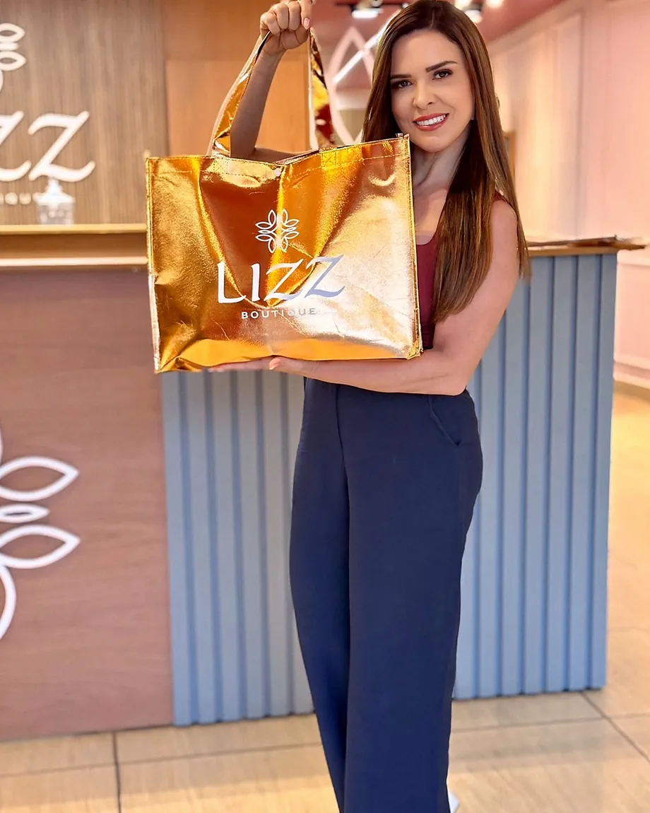 A sacola dourada da Lizz Butique, o brinde entregue na live, nas mãos da Viviane